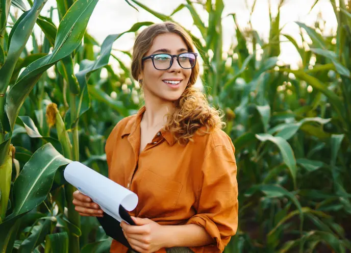 A happy expression women holding a clipboard in a corn field.